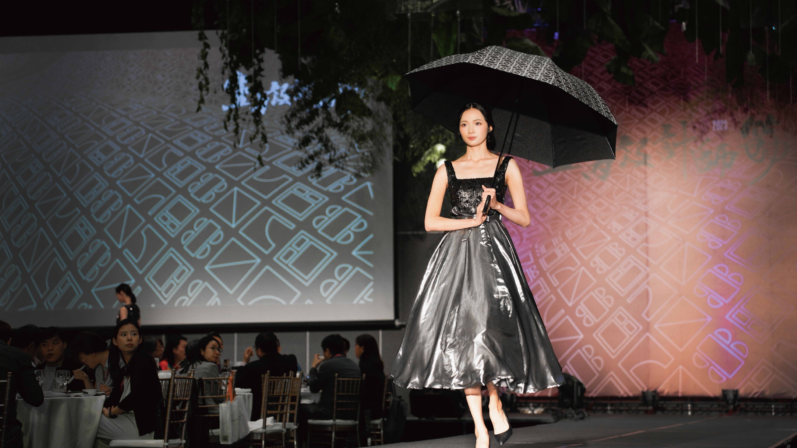 2023 華之金創獎時裝秀：女模持傘身著銀灰亮面澎裙禮服，背板為風光Ai窗窗型元素圖騰投影